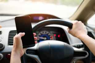 person holding black smartphone and vehicle steering wheel